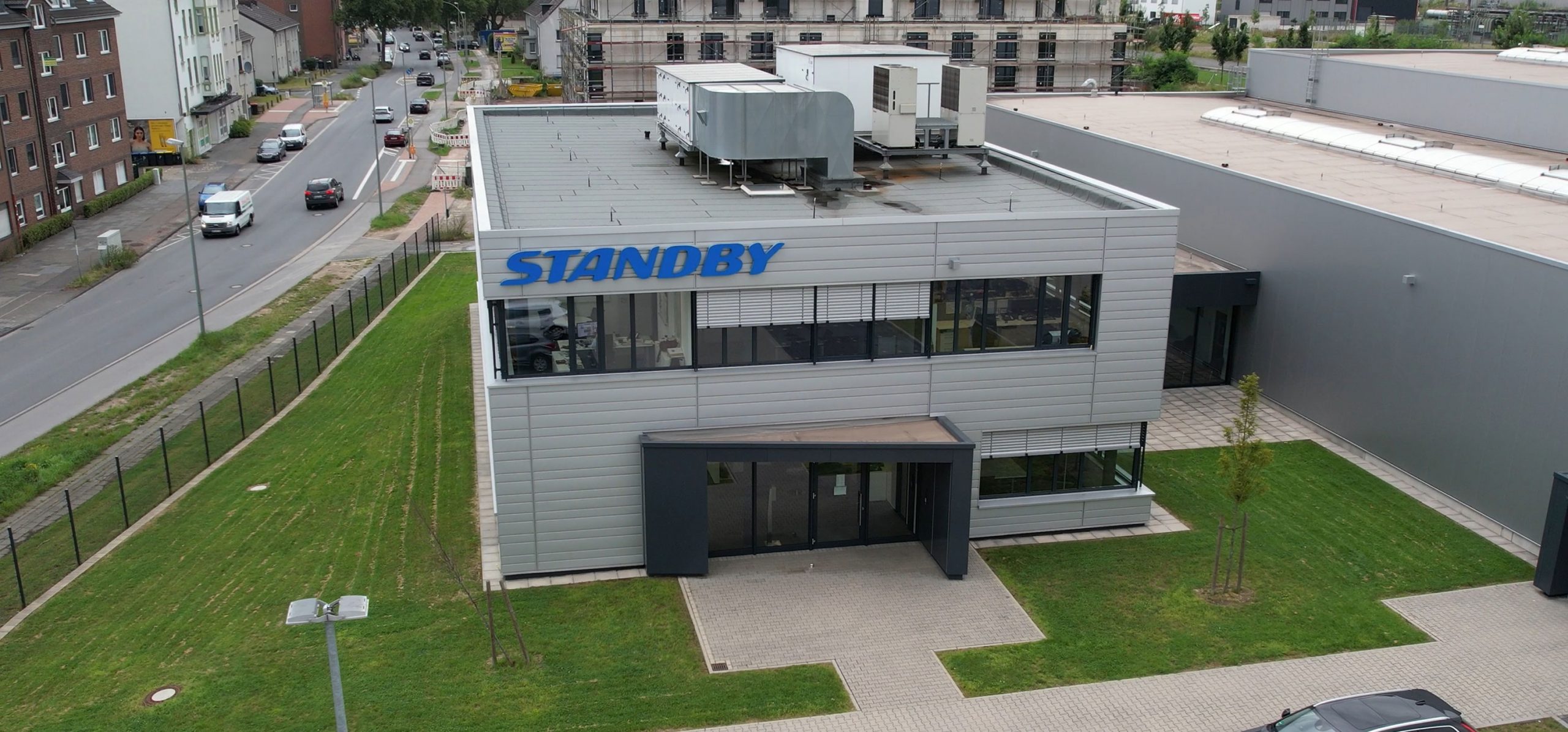 Hero Image Standby Building shown from height, grey panelled building has large blue Standby sign and is surrounded by grass and car park