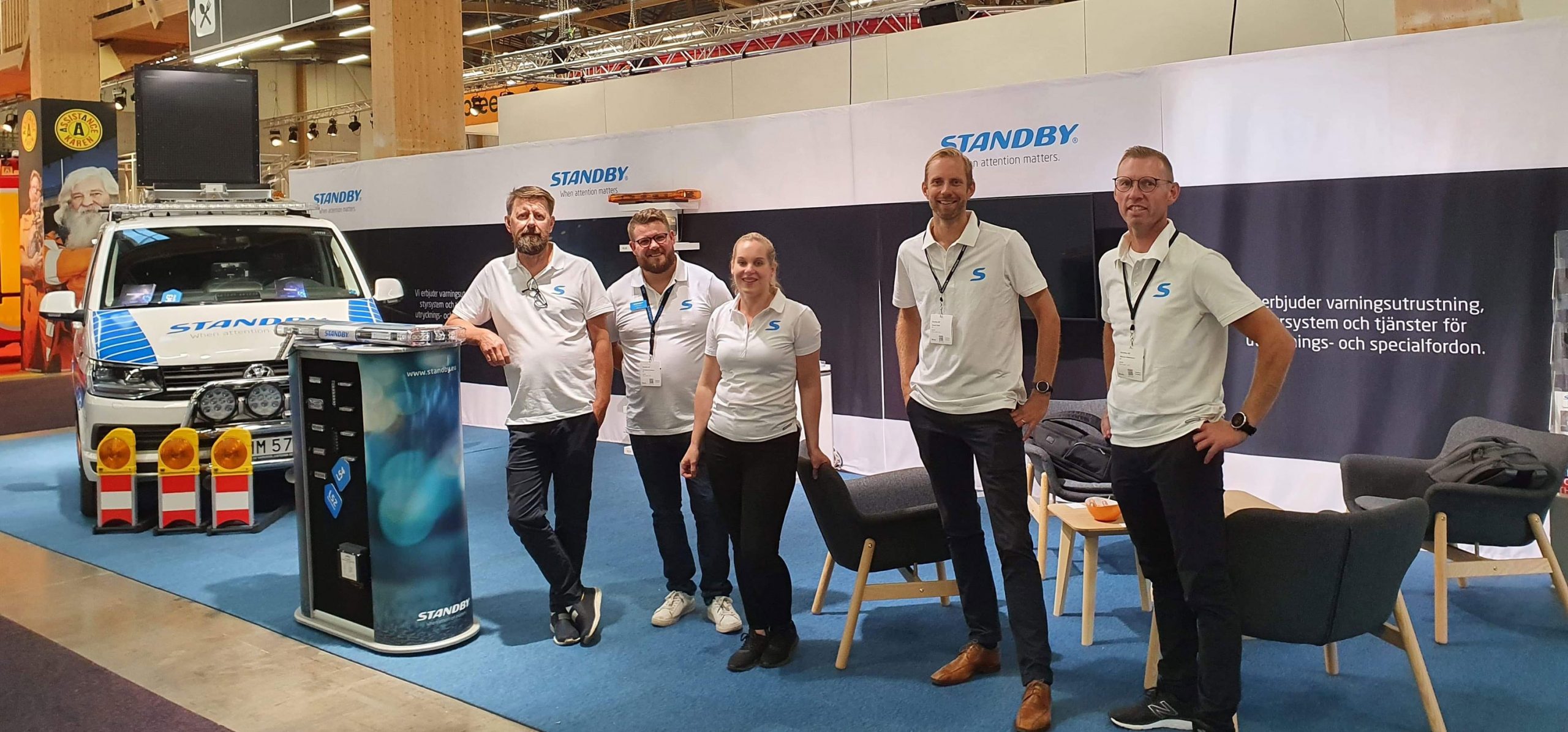 Standby medarbetare med vita skjortor står på rad i en mässmonter. Mässor